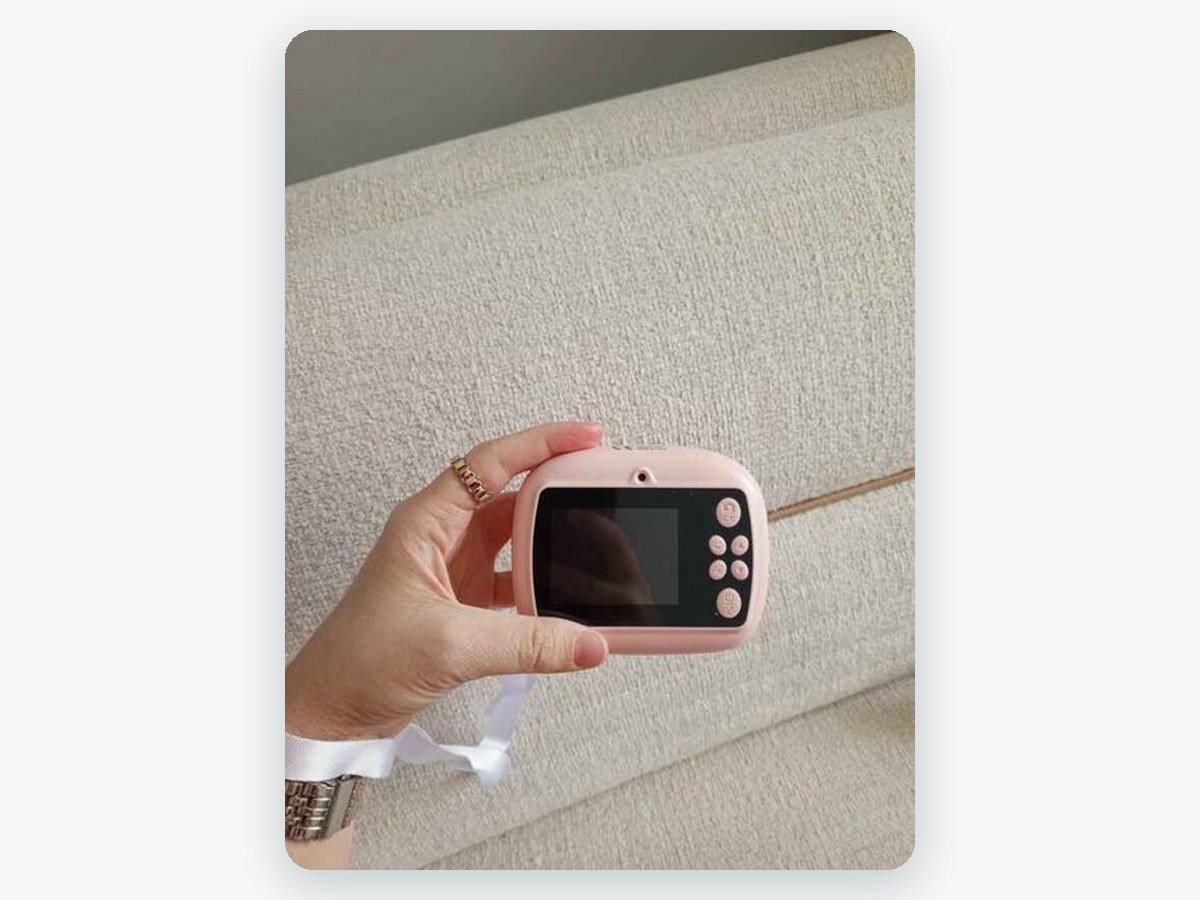 Ebeveynin elinde pembe fotoğraf makinesinin arka yüzü, ekranı, tuşları ve beyaz askı ipi